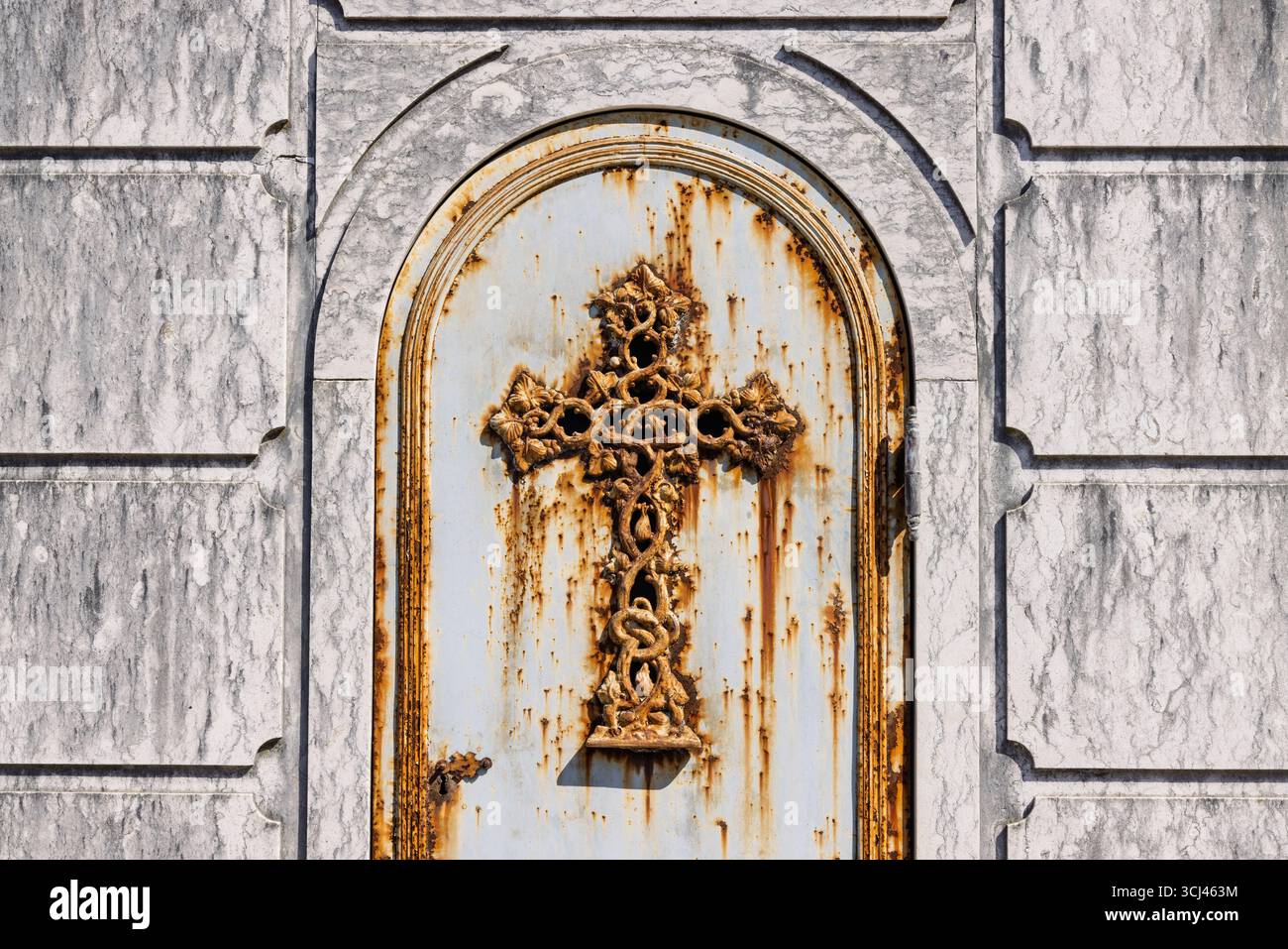 Un'antica porta funeraria con una croce in metallo arrugginito splendidamente ornata. La facciata in marmo mostra la sua età, un netto contrasto con l'intricato ferro Foto Stock
