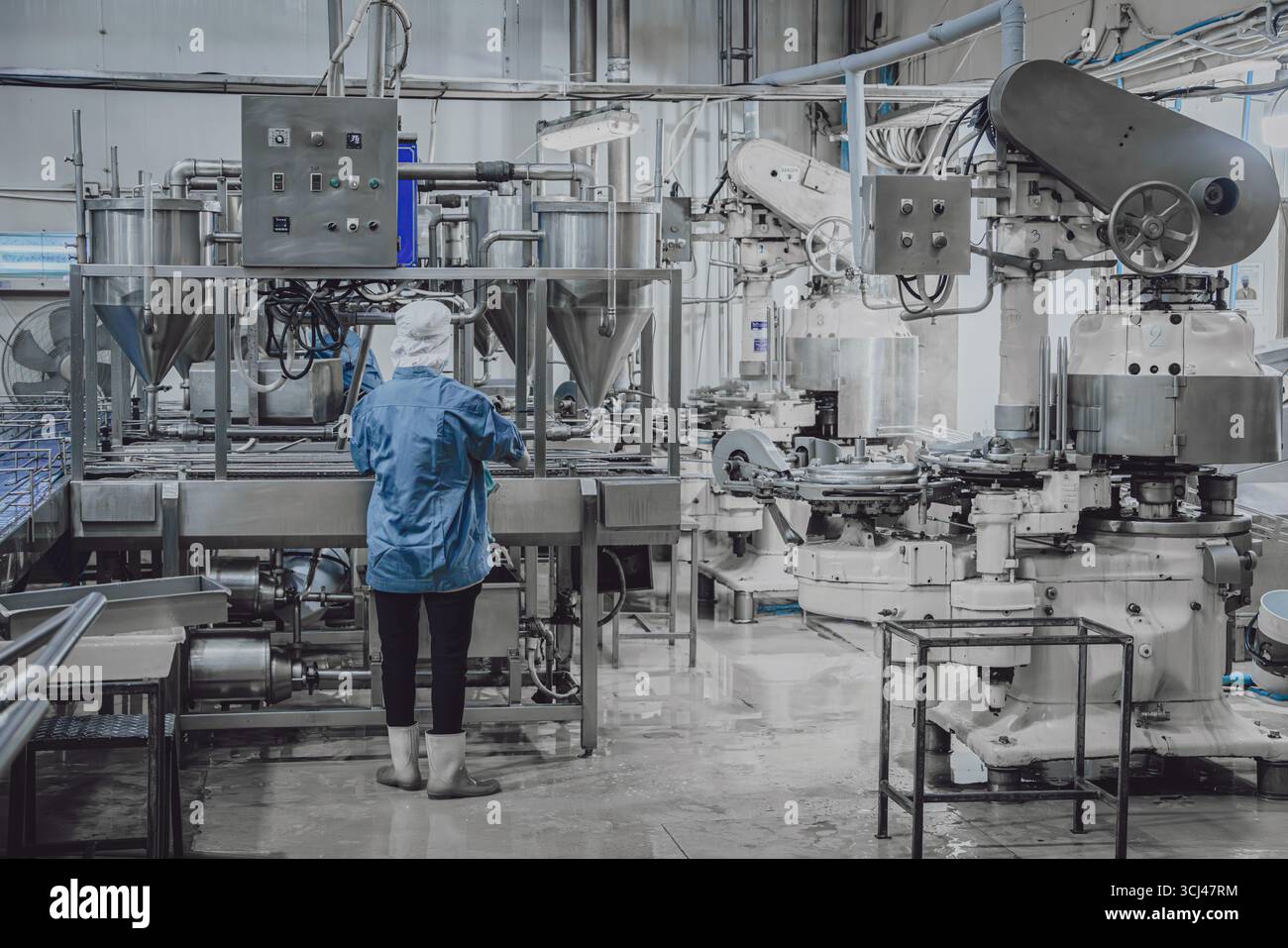 Fabbrica silenziosa, pochi operai che puliscono la linea di produzione trasportano il nastro si preparano a chiudere la fabbrica di alimenti di notte Foto Stock