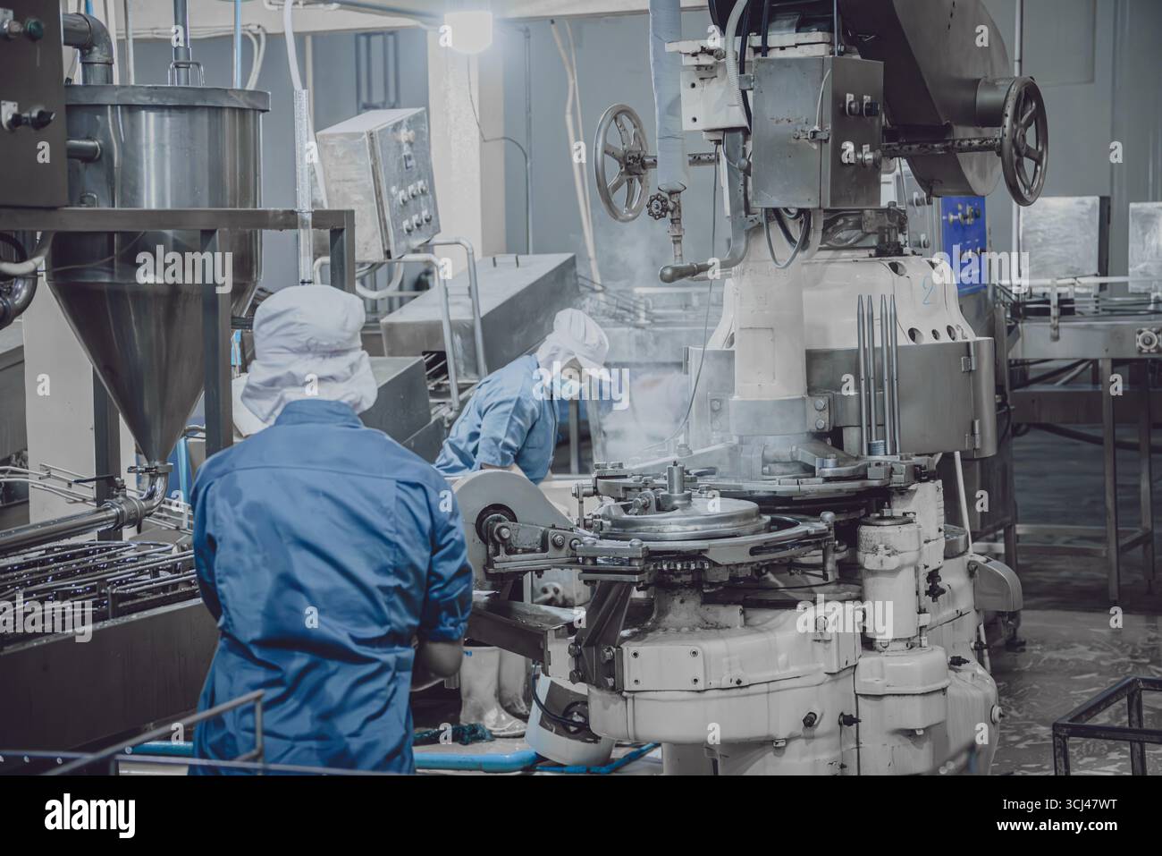 Fabbrica silenziosa, pochi operai che puliscono la linea di produzione trasportano il nastro si preparano a chiudere la fabbrica di alimenti di notte Foto Stock