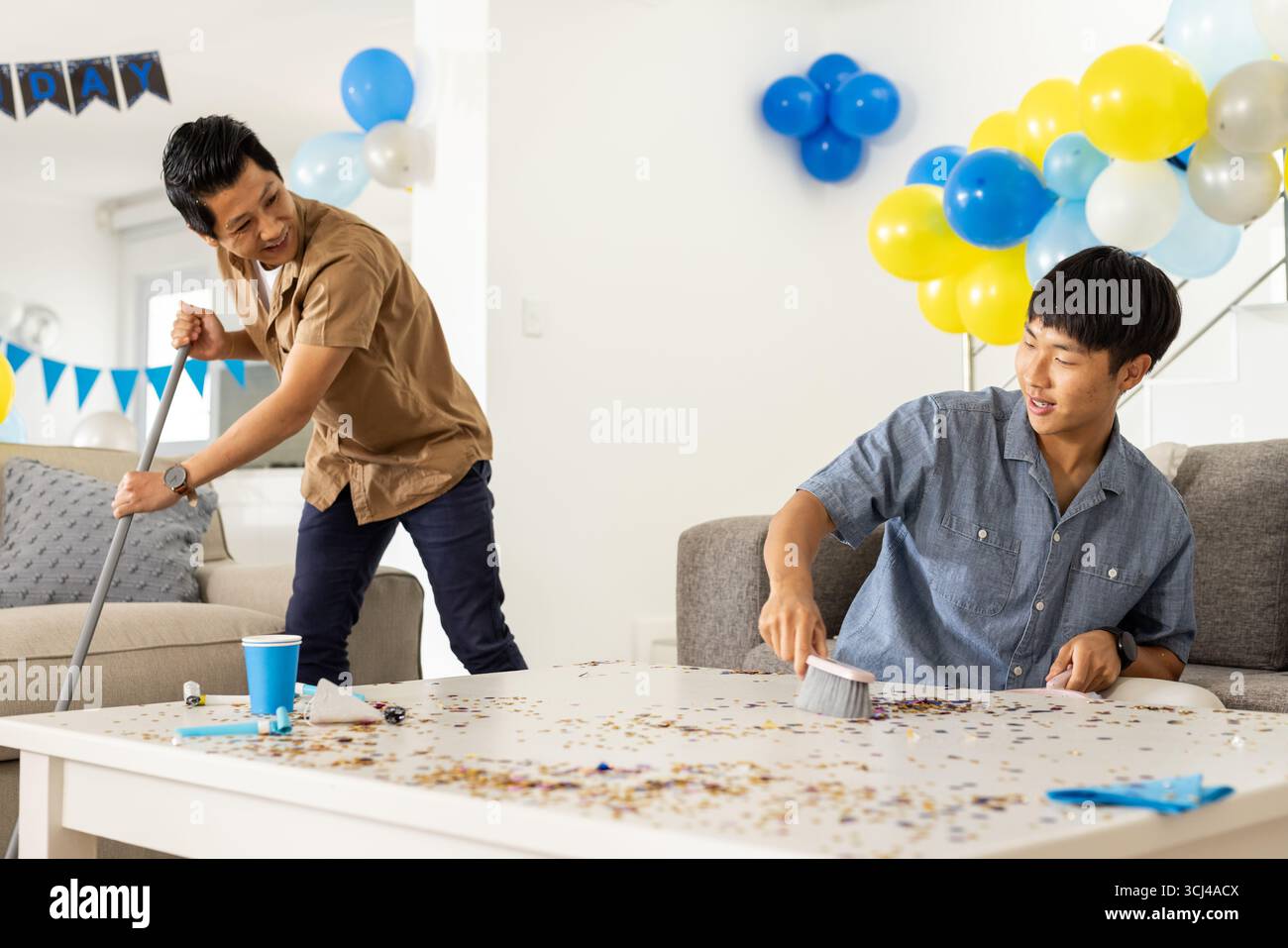 Gli amici ripuliscono i coriandoli in salotto, sorridono e si divertono con il lavoro di squadra Foto Stock