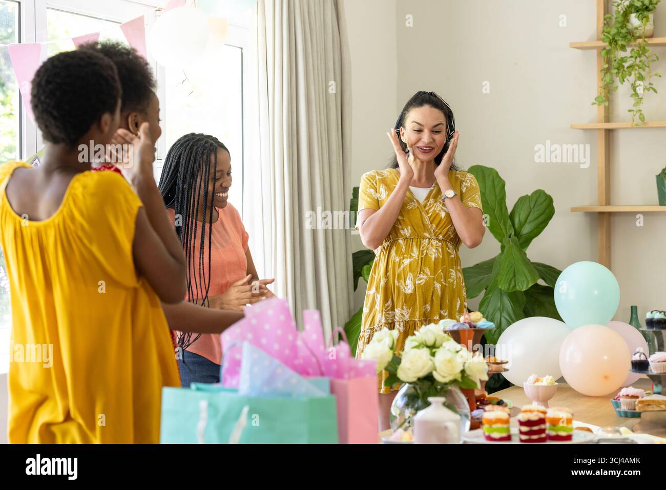 Festeggiamo a casa, amici di sesso femminile diversi che si divertono con una festa a sorpresa con regali Foto Stock