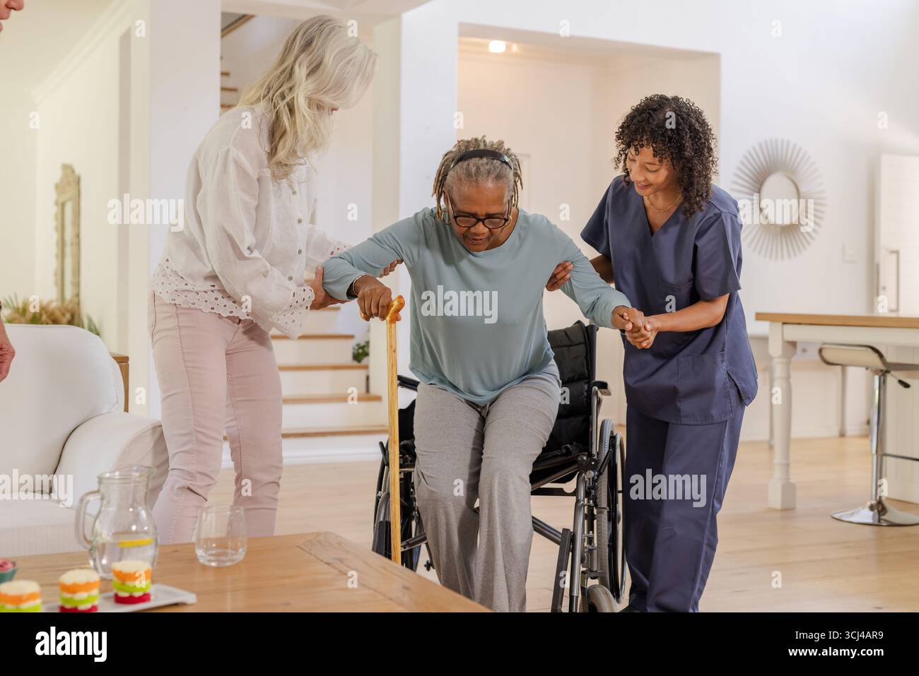 Assistere una donna afroamericana anziana, assistendo gli assistenti nella transizione dalla sedia a rotelle a casa Foto Stock