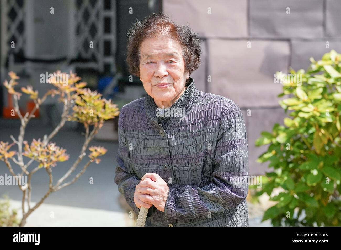 Una donna con una giacca grigia sta tenendo un bastone. Lei sorride ed è felice Foto Stock