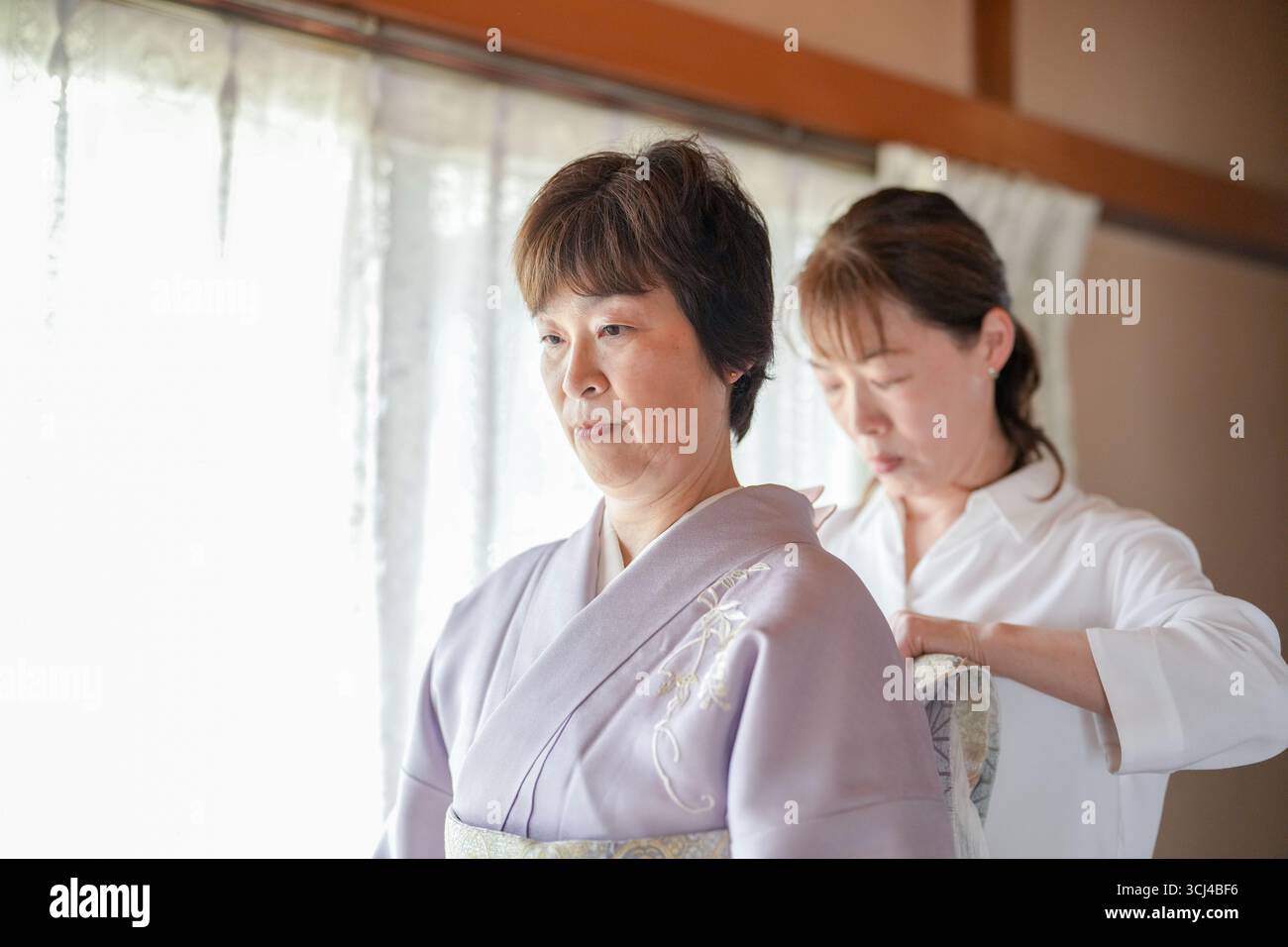 Una donna in un kimono viene aiutata da un'altra donna per regolare i suoi vestiti. Concetto di cura e sostegno tra le due donne Foto Stock