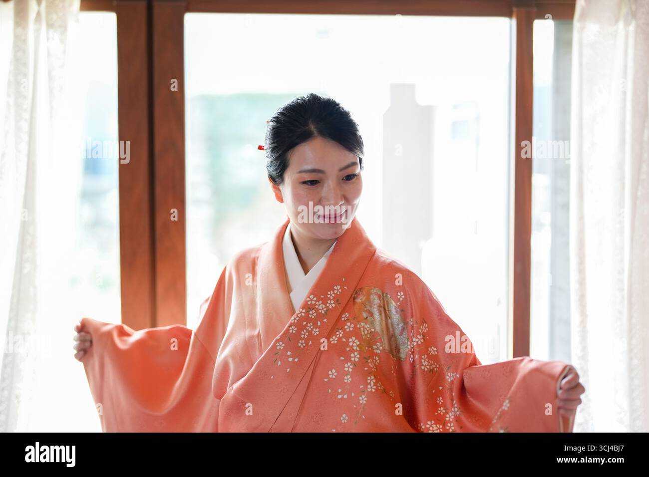 Una donna in un tradizionale kimono giapponese è in piedi davanti a una finestra, sorridente. Concetto di eleganza e apprezzamento culturale, come la donna è dre Foto Stock