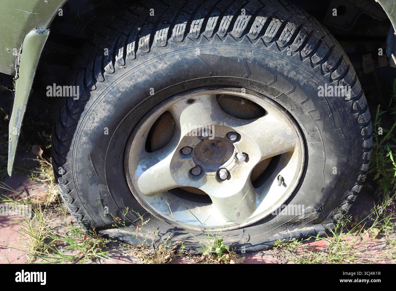 Pneumatico sgonfio su una ruota danneggiata primo piano su fondo stradale esterno concetto di guasto incidente e necessità di riparazione Foto Stock