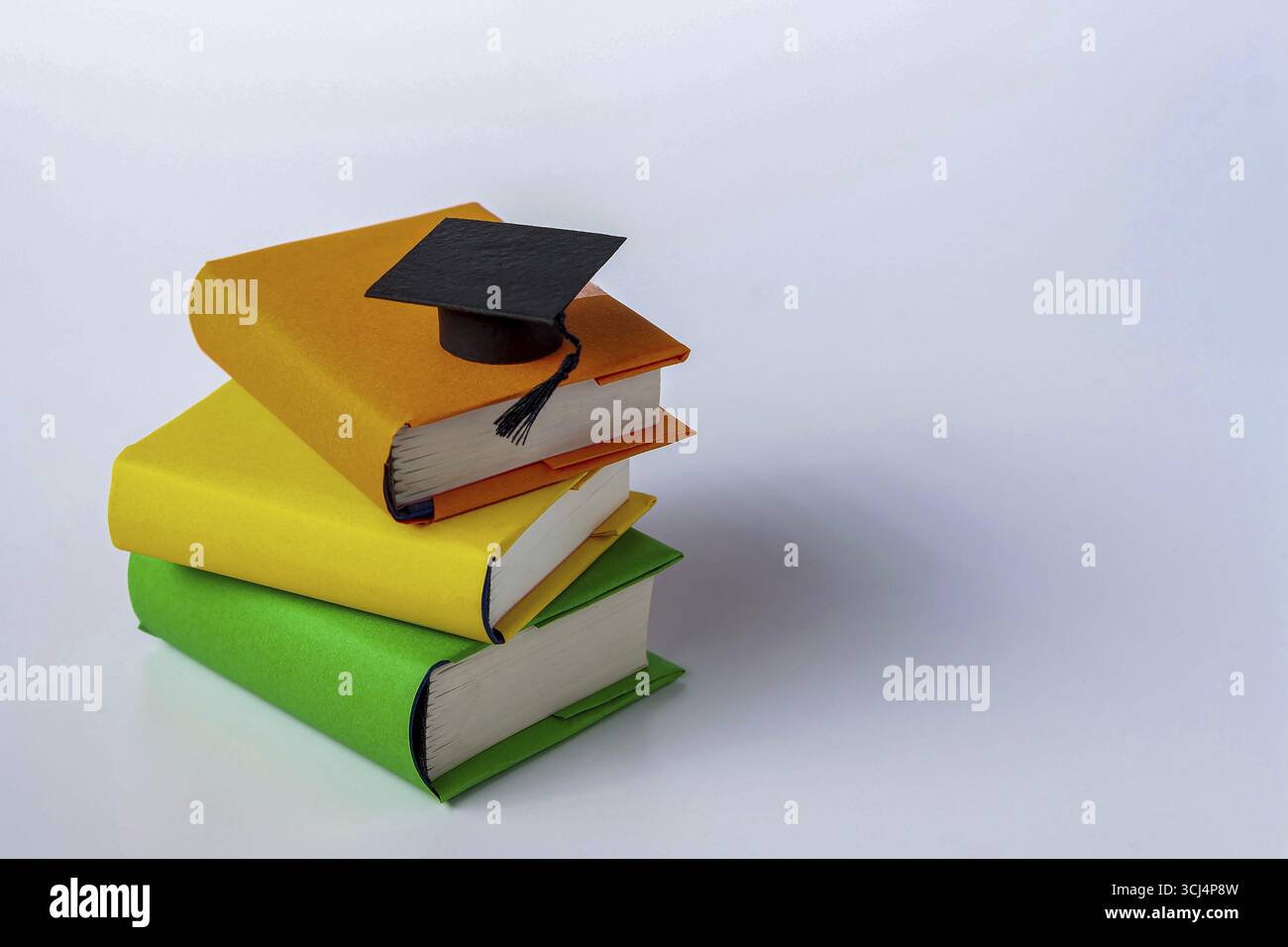 Il cappello da studente giace su una pila di libri colorati Foto Stock