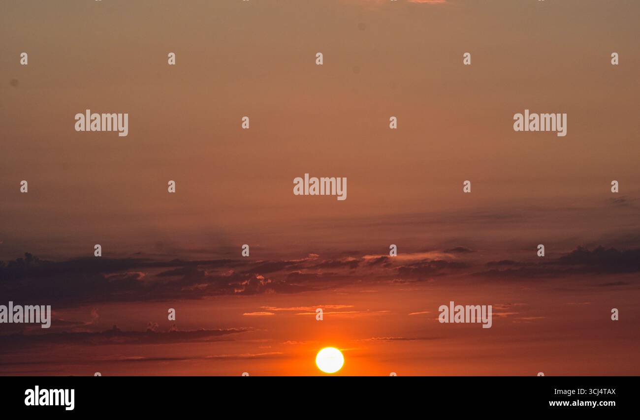 Tramonto con sole incandescente all'orizzonte, cielo magico e colorato pieno di toni caldi, creando un'atmosfera tranquilla e da sogno. Foto Stock