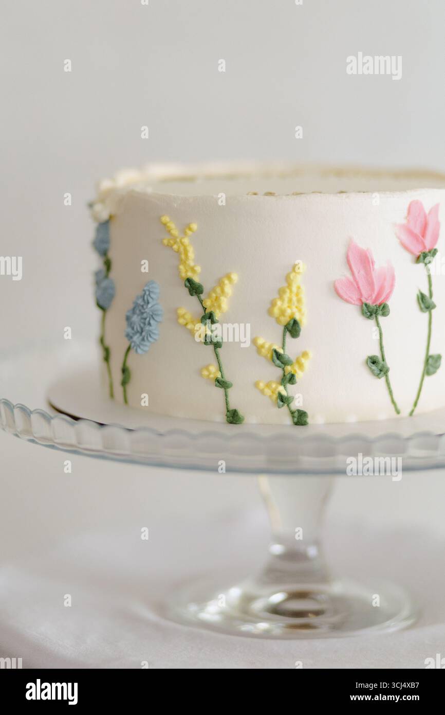 Una torta splendidamente lavorata adornata da fiori colorati di glassa, esposta su un elegante piedistallo in vetro. Foto Stock