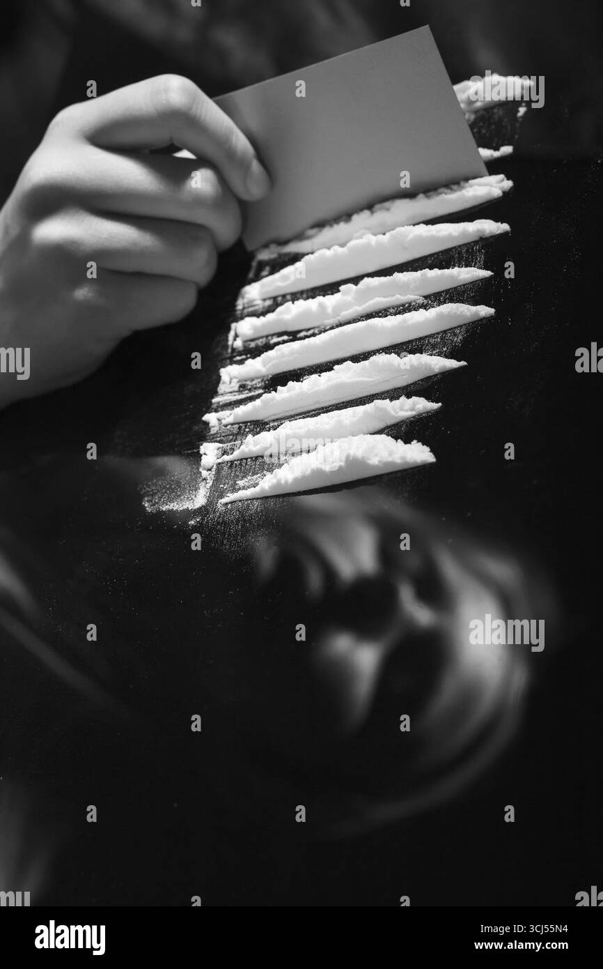 Cocaina o altri farmaci tagliati con carta sullo specchio con riflesso femminile, polvere bianca divisoria a mano narcotica, monocromatica Foto Stock