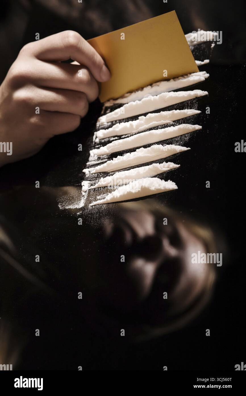 Cocaina o altri farmaci tagliati con carta sullo specchio con riflesso femminile, a mano che divide la polvere bianca narcotica Foto Stock
