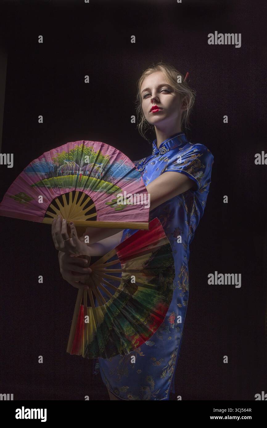 Ragazza in abito asiatico ballare con i fan su sfondo nero Foto Stock