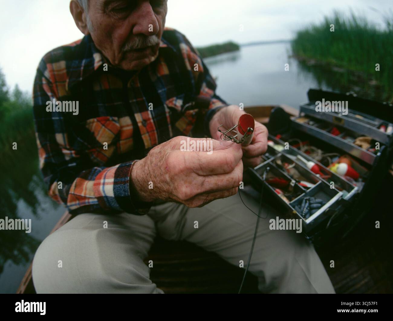Pescatore in pensione seduto sulla sua barca all'alba scegliendo il suo richiamo. Foto Stock