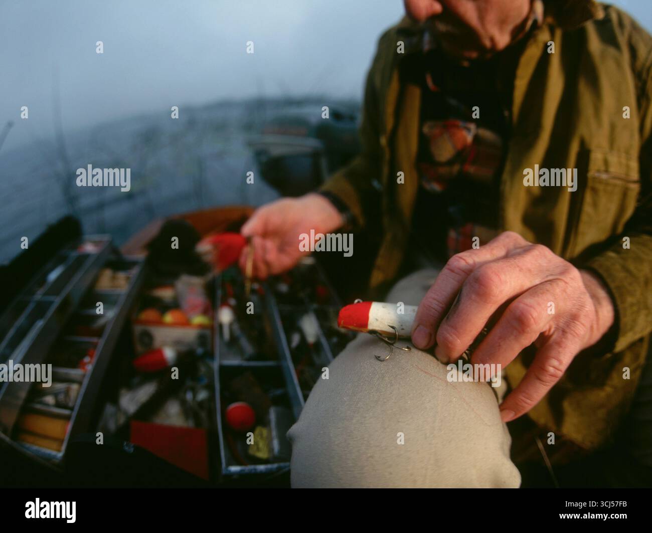 Pescatore in pensione seduto sulla sua barca all'alba scegliendo il suo richiamo. Foto Stock