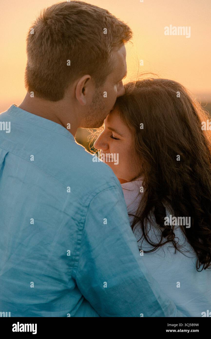 L'uomo bacia delicatamente la fronte di womanÂ durante il tramonto Foto Stock