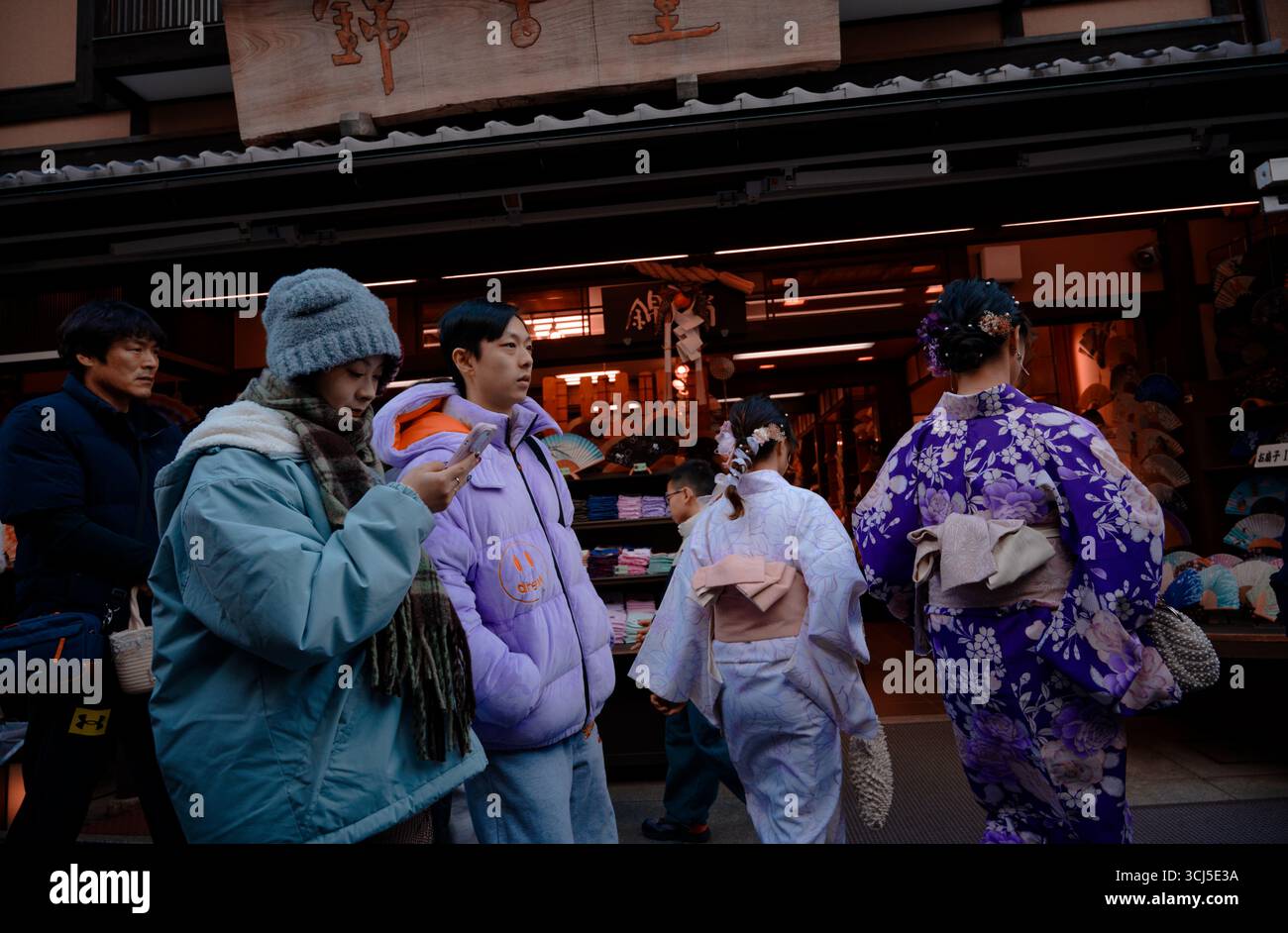 Le donne in kimono entrano in un negozio tradizionale come le altre camici invernali scorrono sul telefono Foto Stock