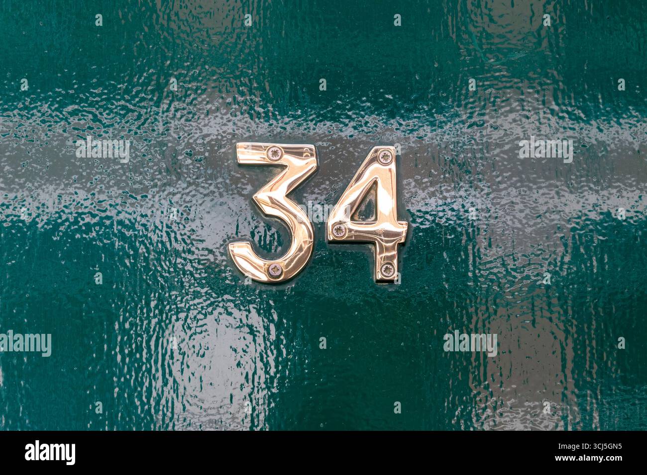Ottone numero trentaquattro su porta verde lucida Foto Stock