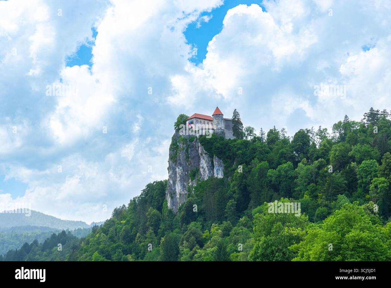 Storico Castello di Bled arroccato su una scogliera sopra la foresta con nuvoloso cielo estivo sullo sfondo Foto Stock