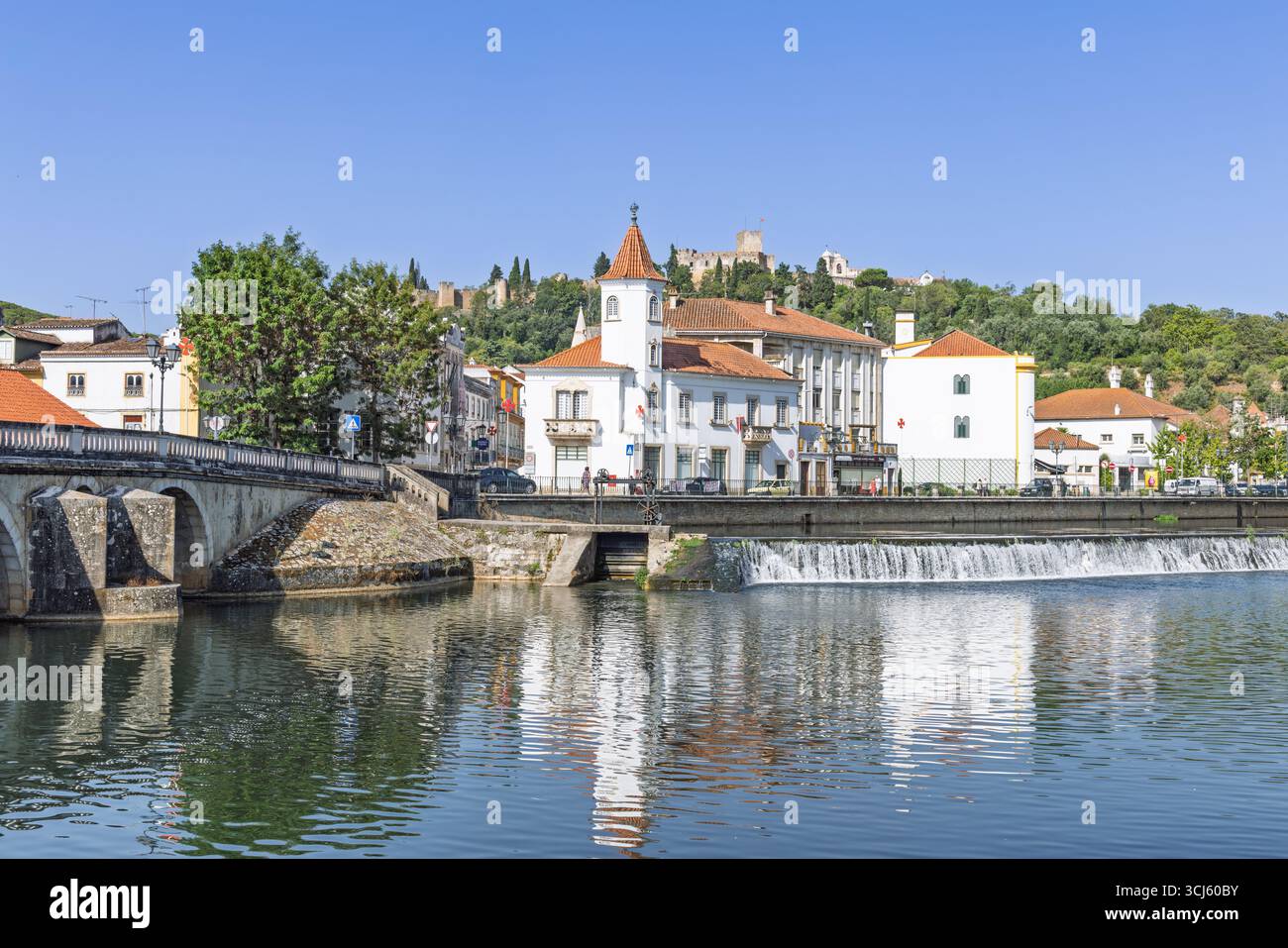 Il tranquillo fiume Nabão scorre oltre un'affascinante città portoghese, con i suoi edifici che si riflettono nelle acque calme. Il maestoso castello di Tomar si trova sulla collina A. Foto Stock