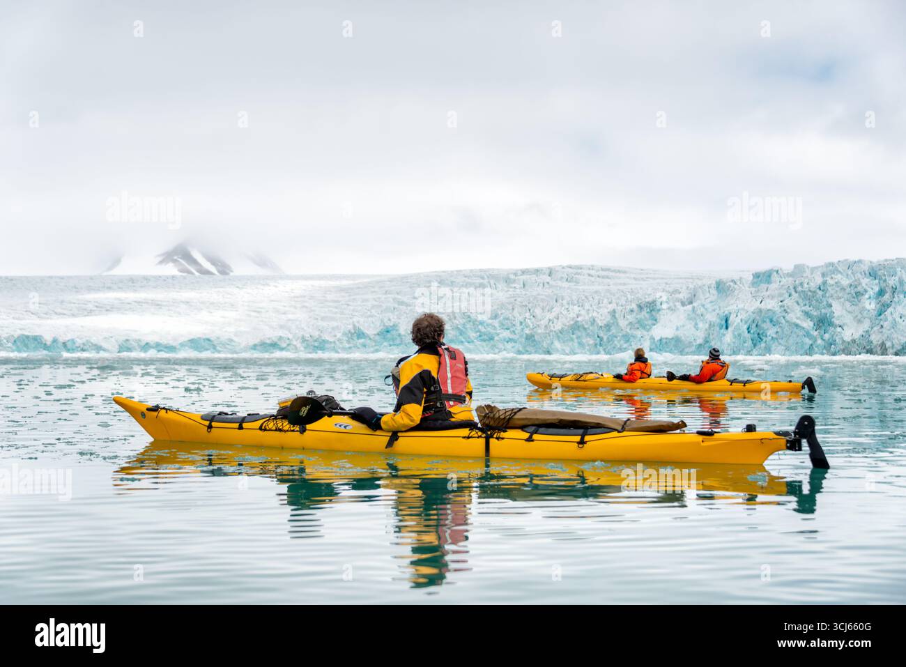 Kayakisti nel Lilliehöökfjorden Spitsbergen Svalbard Norvegia | SPITSBERGEN, Svalbard — Kayakisti con equipaggiamento ad alta visibilità giallo e arancione navigano attraverso acque cosparse di ghiaccio davanti all’estesa fronte di calata del Lilliehökbreen nel Lilliehöökfjorden. Il ghiacciaio, una composizione di più di dieci torrenti glaciali tributari che drenano la Terra di Alberto I, si è ritirato con una velocità media di più di 330 piedi (100 m) all’anno dal 2000, un tasso tra i meglio documentati sulla costa occidentale di Svalbard. Foto Stock