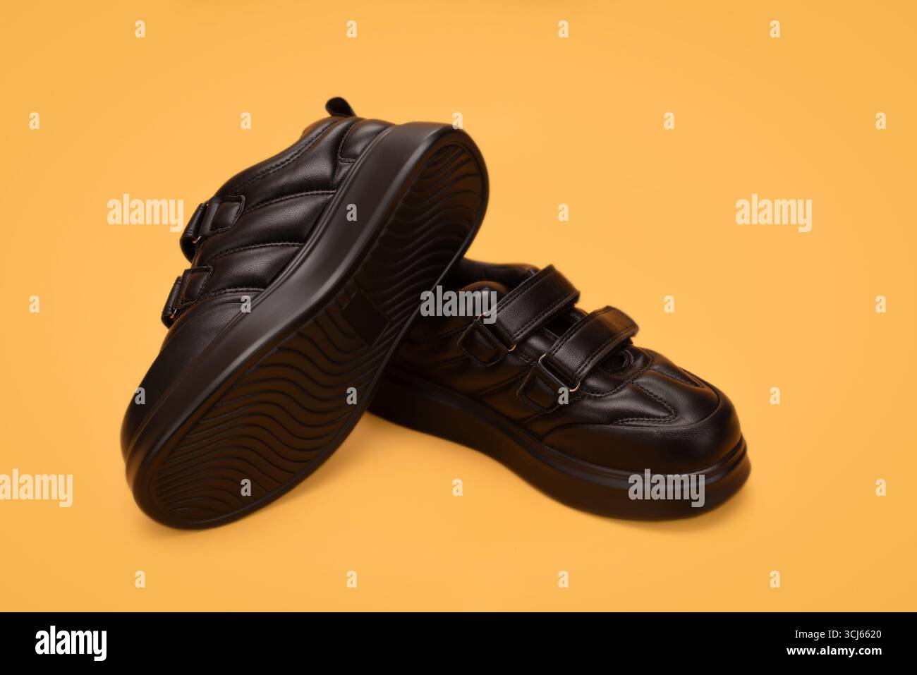 Primo piano di moderne scarpe in pelle nera con cinturini in velcro su uno sfondo giallo brillante. Perfetto per temi di moda, stile e calzature, per camminare Foto Stock