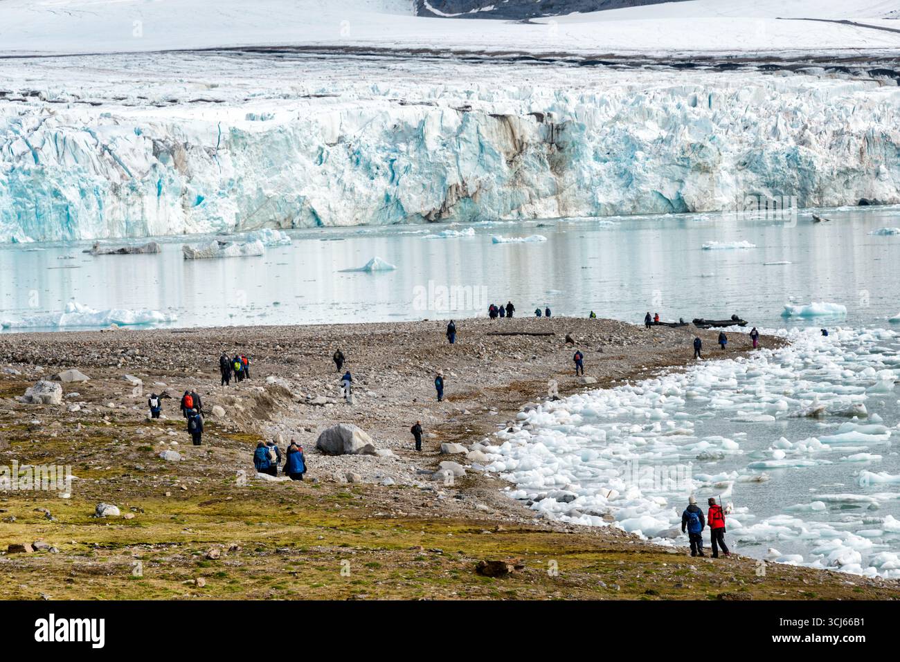 Ghiacciaio Lilliehöökfjorden Spitsbergen Svalbard Norvegia // SPITSBERGEN, Svalbard — Una grande faccia glaciale domina lo sfondo di Lilliehöökfjorden, con un corpo d'acqua pieno di iceberg in primo piano. I turisti possono passeggiare lungo la costa rocciosa e osservare il paesaggio glaciale. Lilliehöökfjorden è un fiordo situato sulla costa occidentale di Spitsbergen, la più grande isola dell'arcipelago delle Svalbard in Norvegia. La regione è conosciuta per le sue spettacolari formazioni glaciali e la fauna selvatica artica. Foto Stock