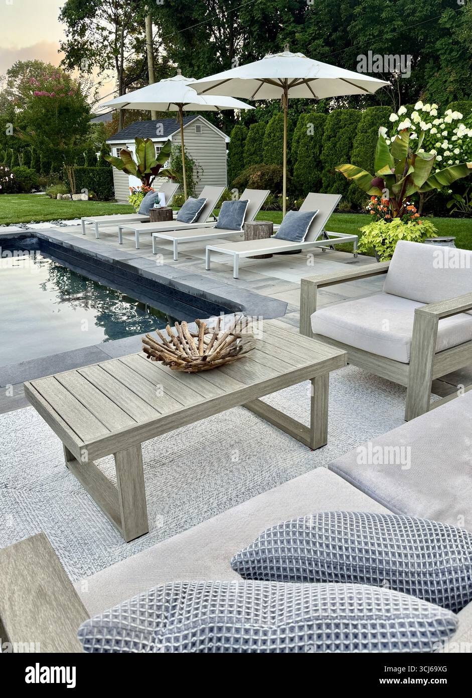 Area lounge con patio e piscina sul retro di lusso e design moderno. Ombrellone, divano, sedie a sdraio, tavolo a bordo piscina. Posti a sedere e solarium con asfaltatrici in pietra grigia. Foto Stock