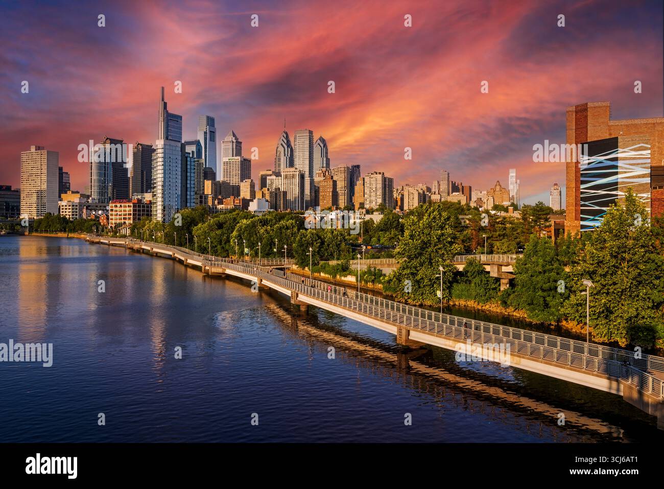 Lo skyline di Filadelfia si illumina sotto un tramonto mozzafiato, con gli edifici iconici della città riflessi nelle tranquille acque sottostanti. Foto Stock
