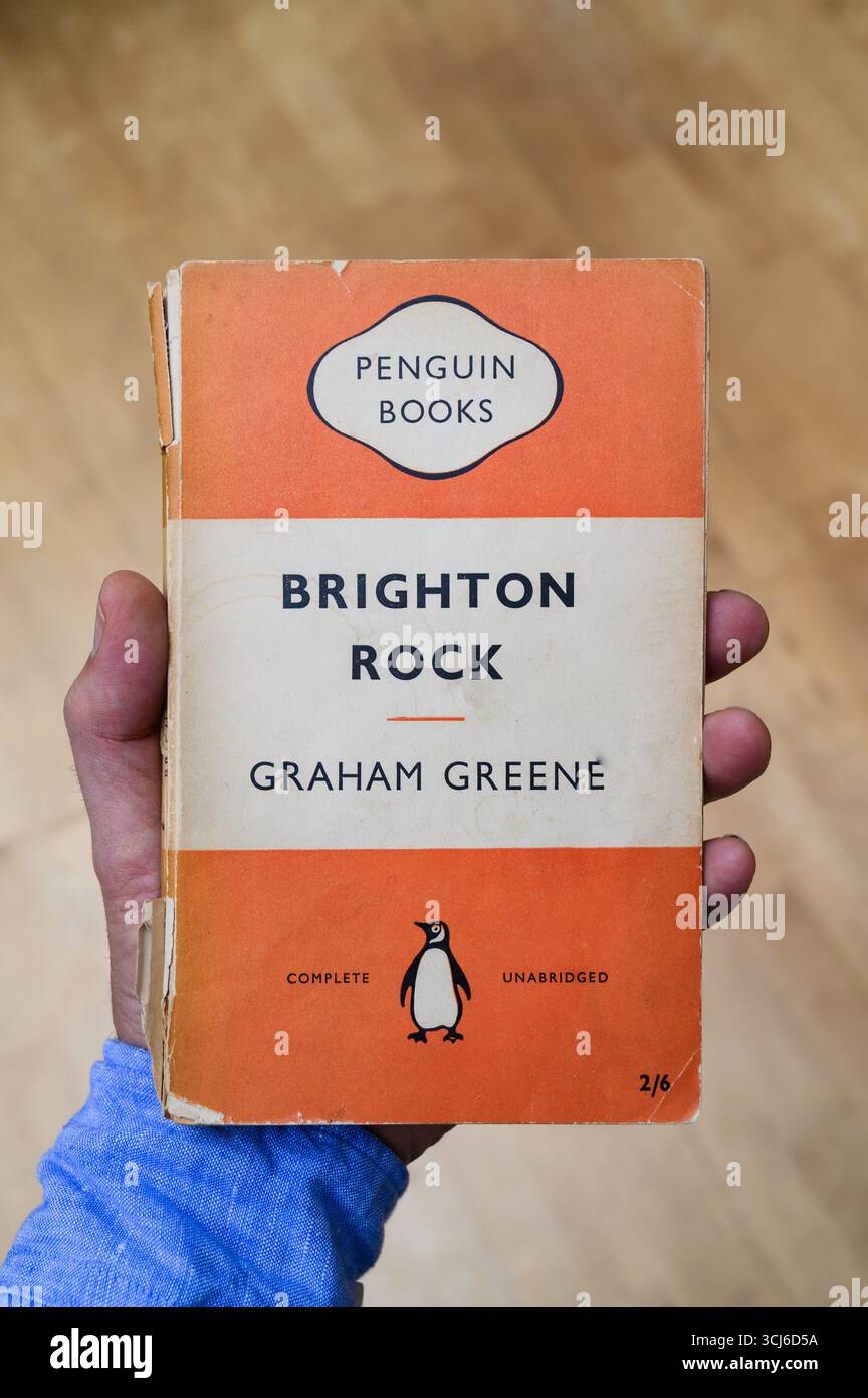 Mano che regge una vecchia edizione dei pinguini di Brighton Rock di Graham Greene Foto Stock