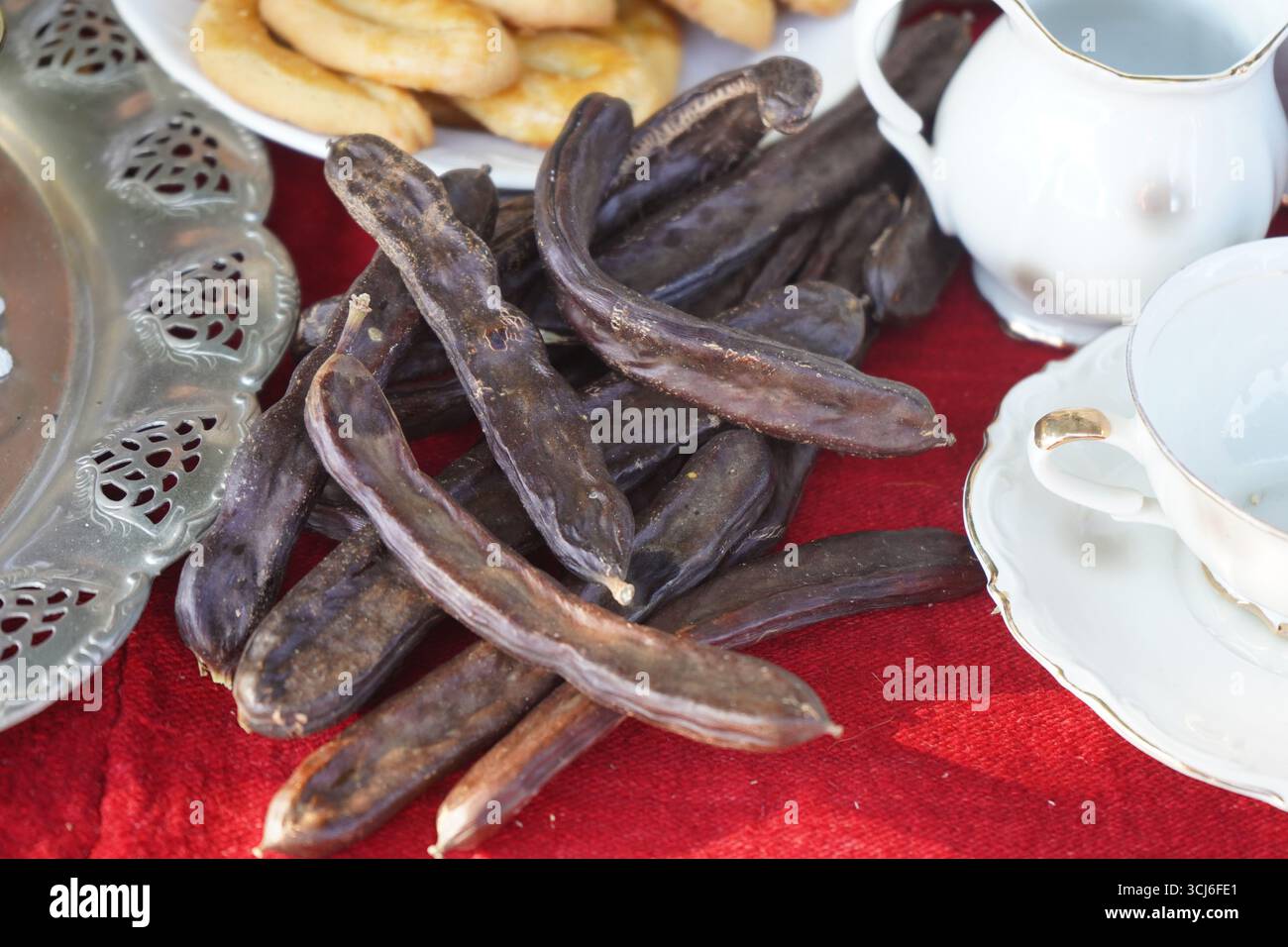 Primo piano di cialde di carruba, un tradizionale superfood cretese, disposte su una rustica tovaglia rossa insieme a tazze da tè e dolci vintage. Foto Stock