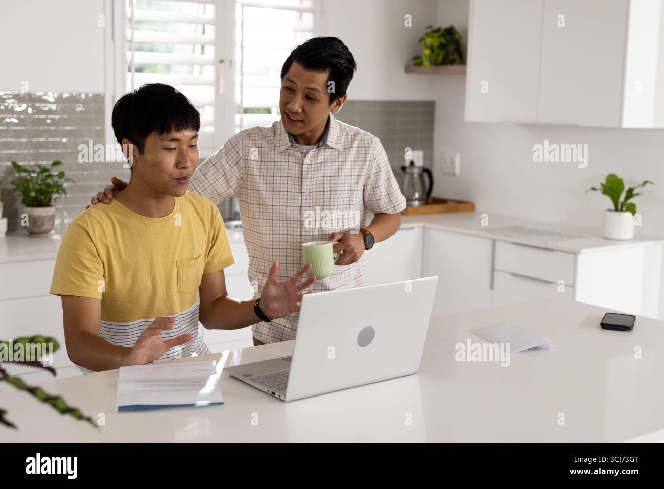 Padre e figlio discutono delle finanze a casa, utilizzando laptop e documenti Foto Stock