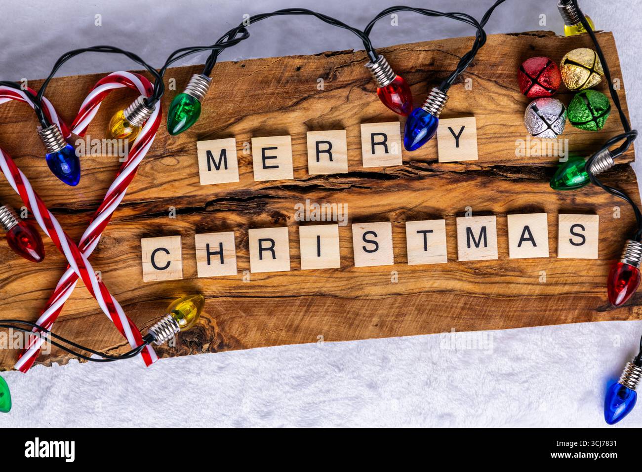 Buon Natale scritto utilizzando piastrelle di lettere di legno su uno sfondo rustico in legno; circondato da colorate luci natalizie; bastoncini di caramelle; e festivi Foto Stock