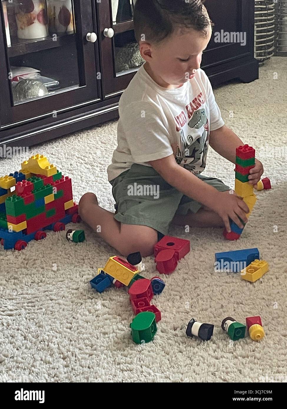 Un bambino di tre anni gioca felicemente con i Lego nel soggiorno di una casa residenziale, 2025, Stati Uniti Foto Stock