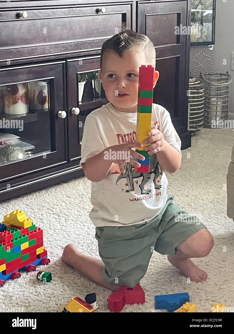 Un bambino di tre anni gioca felicemente con i Lego nel soggiorno di una casa residenziale, 2025, Stati Uniti Foto Stock