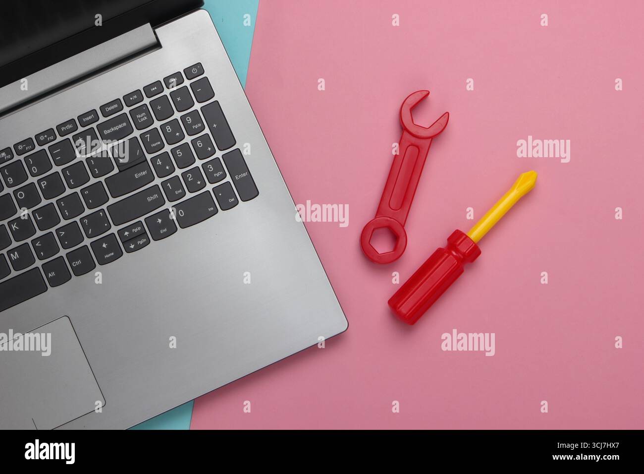 Composizione piatta. Concetto di riparazione. Computer portatile con utensili da lavoro giocattolo su sfondo rosa blu pastello. Vista dall'alto Foto Stock