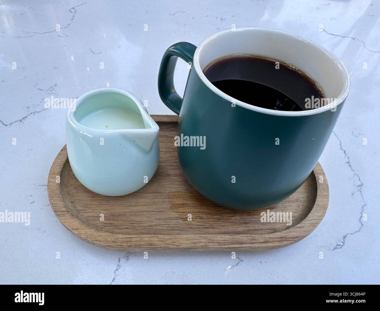 Una tazza di caffè nero con una piccola caraffa di latte servita su un vassoio di legno su una superficie in marmo. Foto Stock