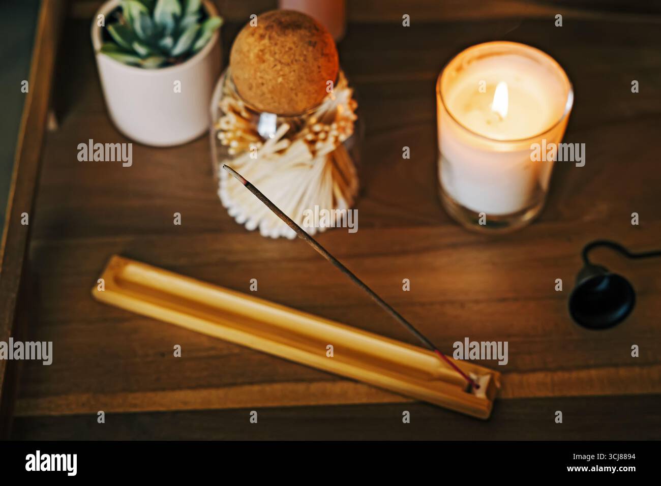 Un ambiente accogliente con un bastoncino di incenso acceso in un supporto accanto a una candela illuminata, per creare un'atmosfera serena e aromatica. Foto Stock