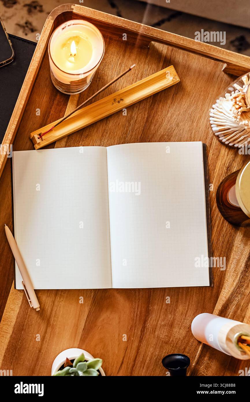 Accogliente area di lavoro per il diario o la meditazione con un quaderno aperto su un vassoio di legno circondato da candele profumate e incenso Foto Stock