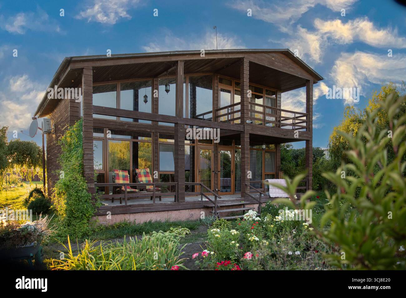 Moderna casa in legno a due piani con grandi finestre circondate da un giardino verde e fiori che creano un'accogliente atmosfera di campagna Foto Stock
