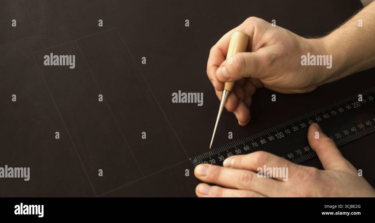 Artigiano che utilizza punteruolo e righello per disegnare linee precise sulla superficie in pelle per la realizzazione di accessori fatti a mano Foto Stock