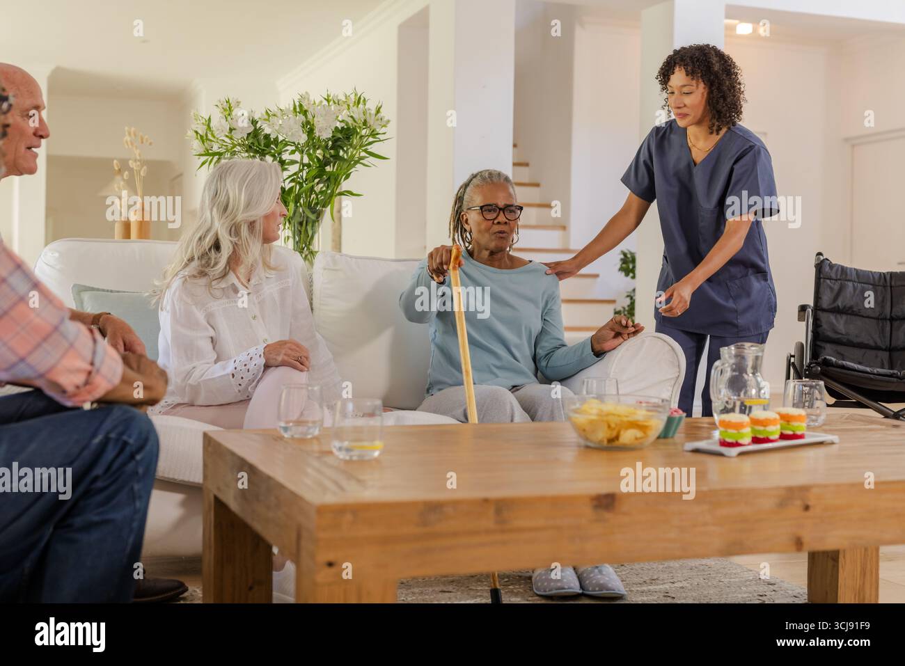 Amici anziani che si divertono a conversare a casa con l'assistenza di un operatore sanitario Foto Stock