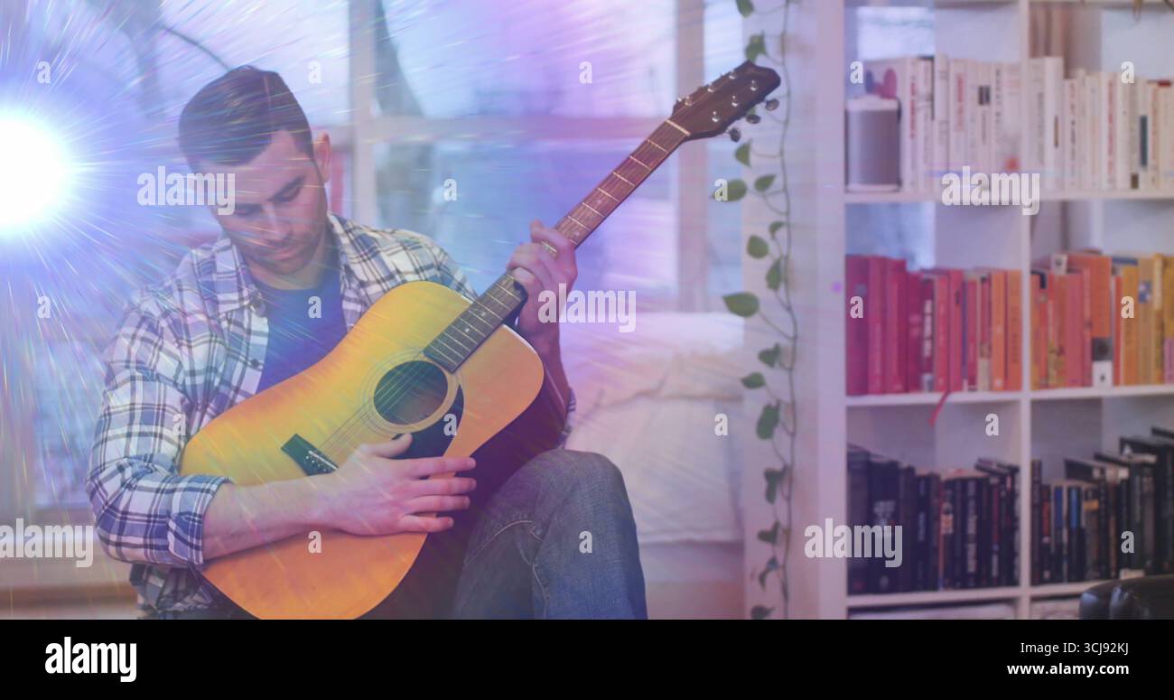 Musicista che suona la chitarra acustica sul pavimento della camera da letto, con piante di vite e libreria bianca Foto Stock