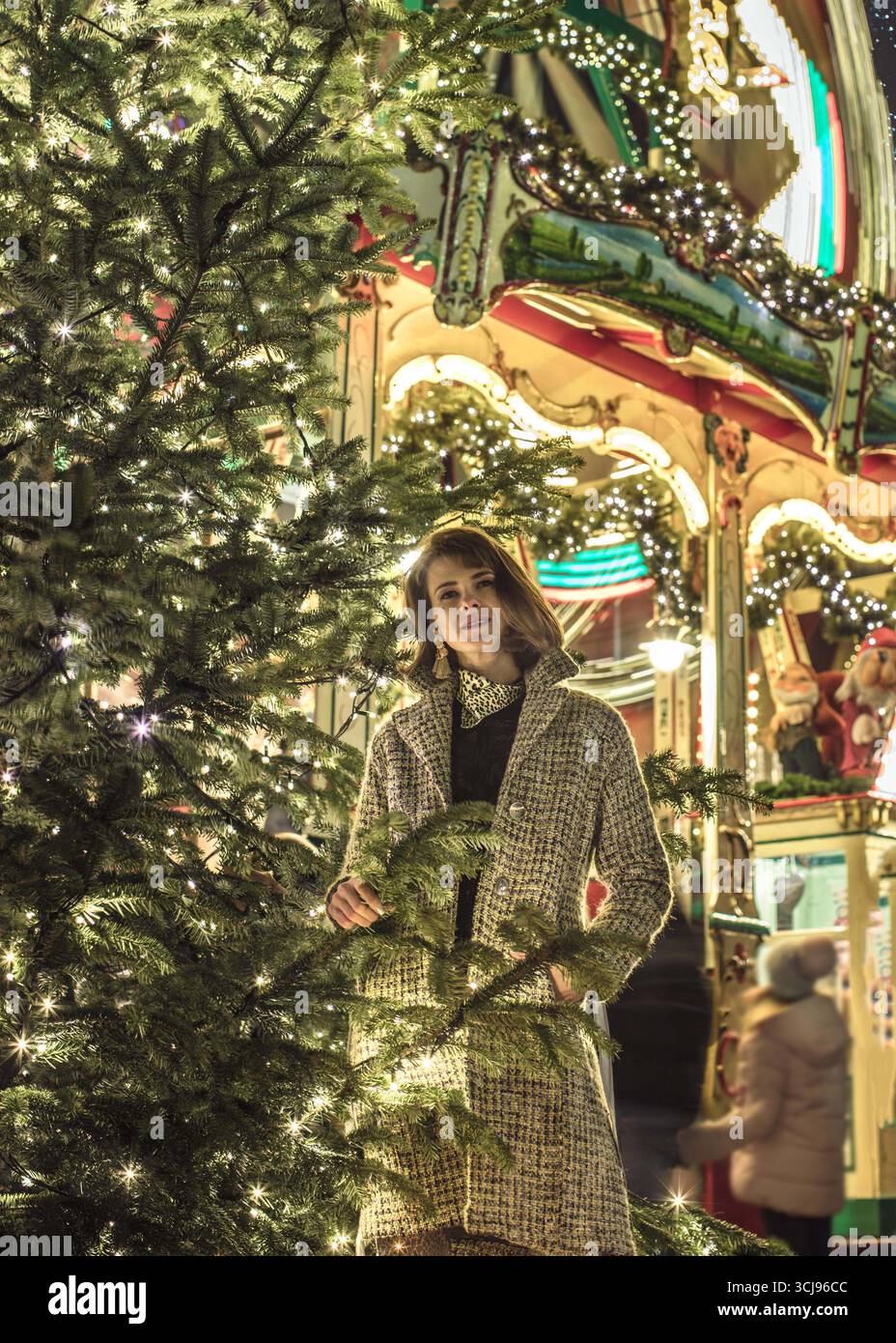 Dietro di lei c'è una bella donna alla moda accanto al mercatino di Natale decorato. Fotografata lunga esposizione di notte. Foto Stock