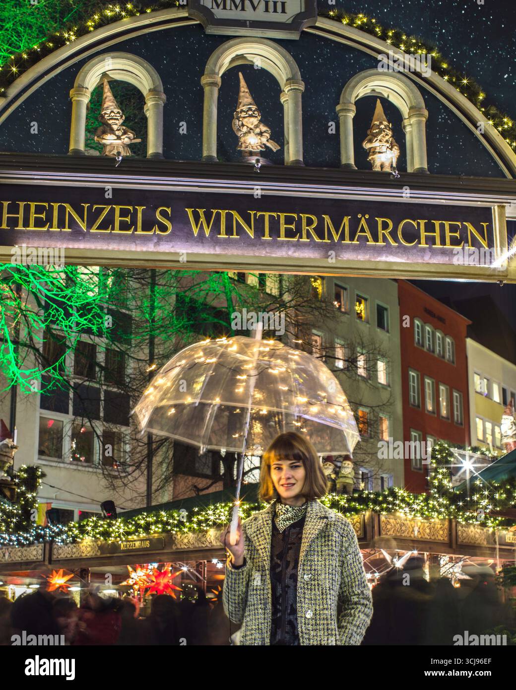 Bella donna alla moda in piedi all'ingresso del mercato di Natale con scritto "Heinzels Wintermärchen" sopra la testa, tenendo in mano l'ombrello. Foto Stock