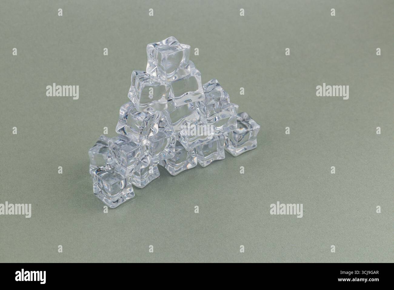 I cubetti di ghiaccio trasparente sono accuratamente impilati in una formazione piramidale su una superficie grigia, mostrando la loro trasparenza e disposizione geometrica in un di unico Foto Stock