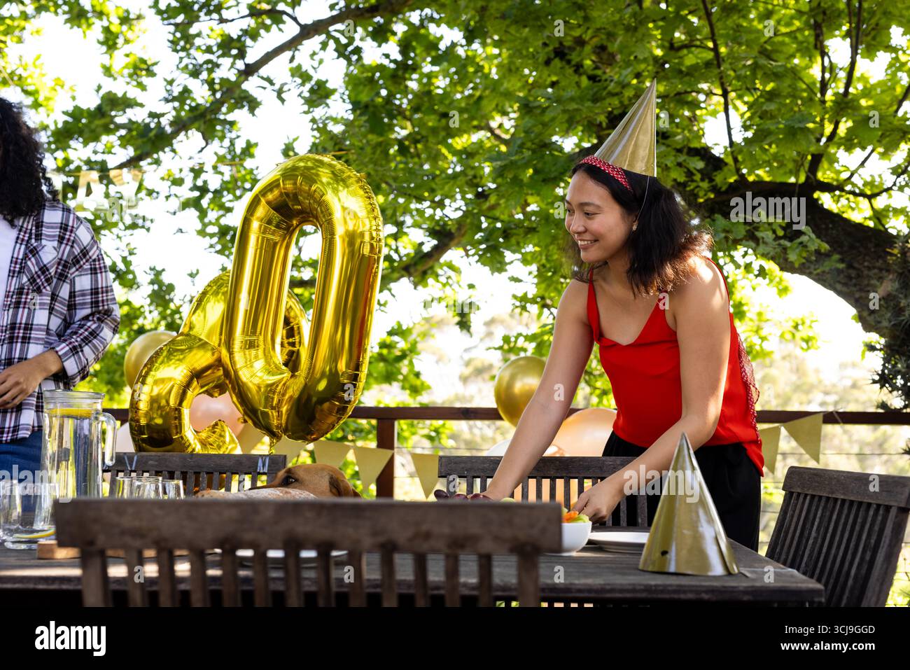 Tavolo all'aperto, donna in abito rosso che organizza il compleanno con palloncini Foto Stock