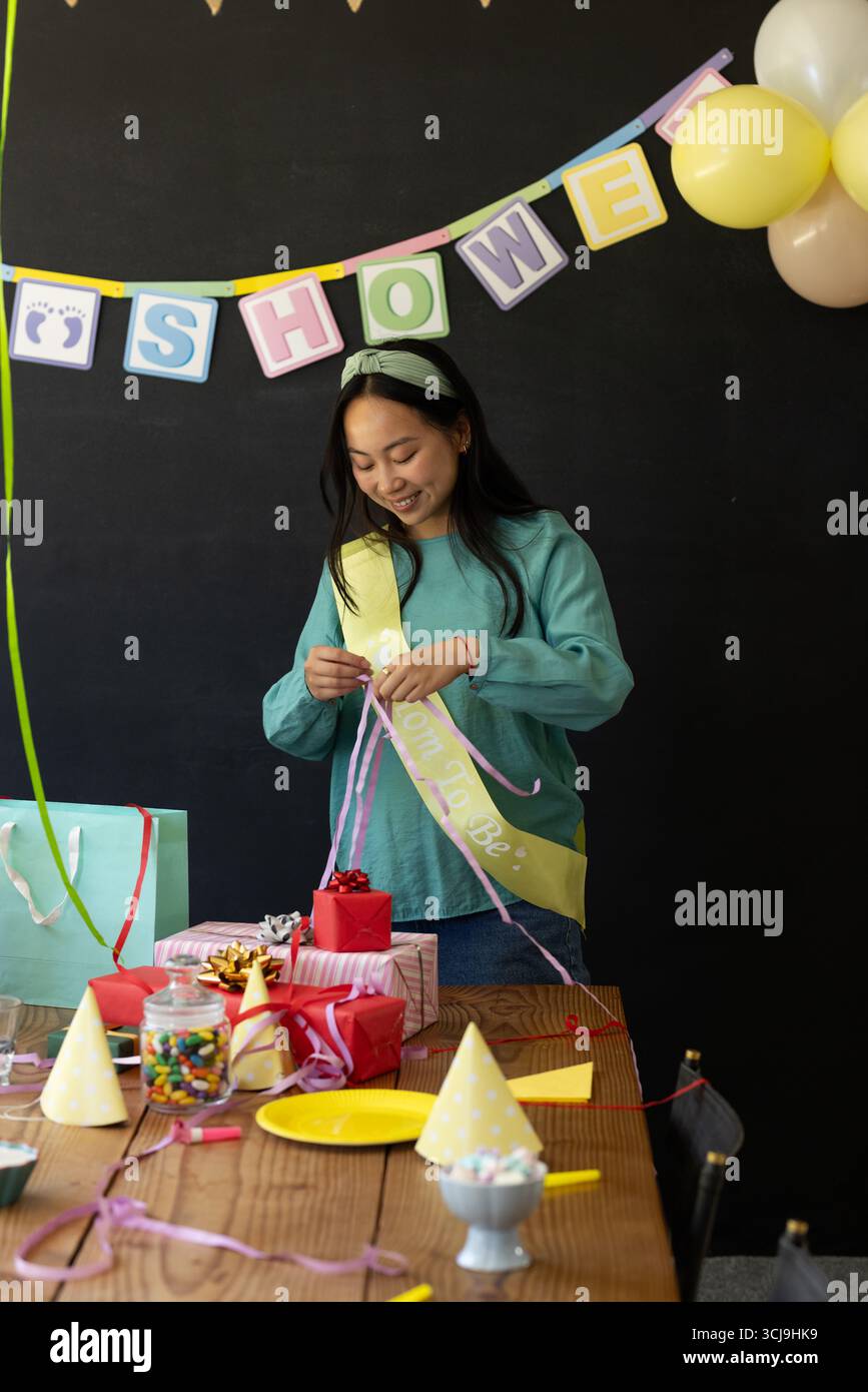 Donna sorridente che prepara regali alla festa con baby shower con decorazioni colorate Foto Stock