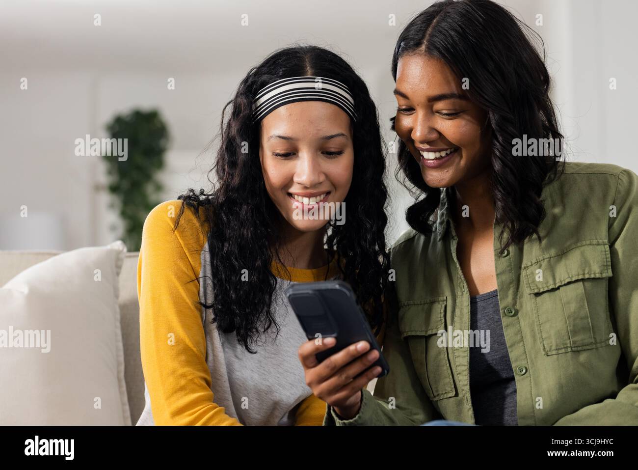 Madre e figlia sorridono mentre guardano lo smartphone insieme a casa Foto Stock