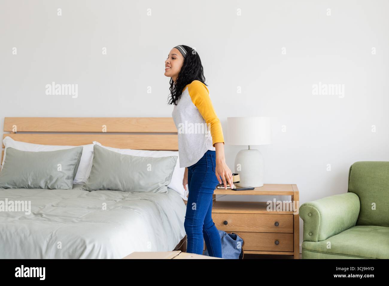 Donna sorridente in camera da letto che regge lo smartphone, godendo momenti di relax Foto Stock