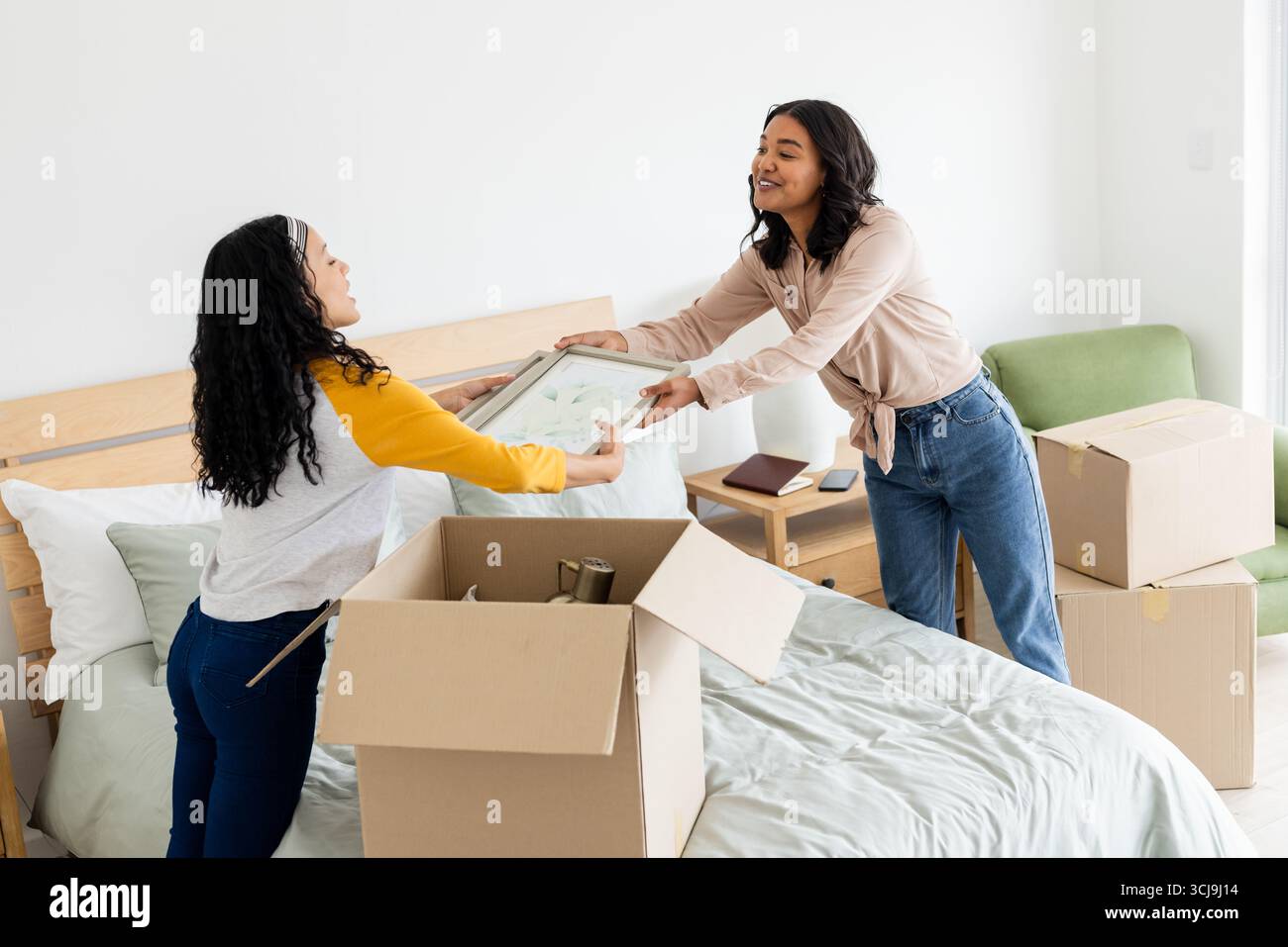 Due donne che disimballano le scatole sul letto, sorridono e organizzano una nuova casa insieme Foto Stock